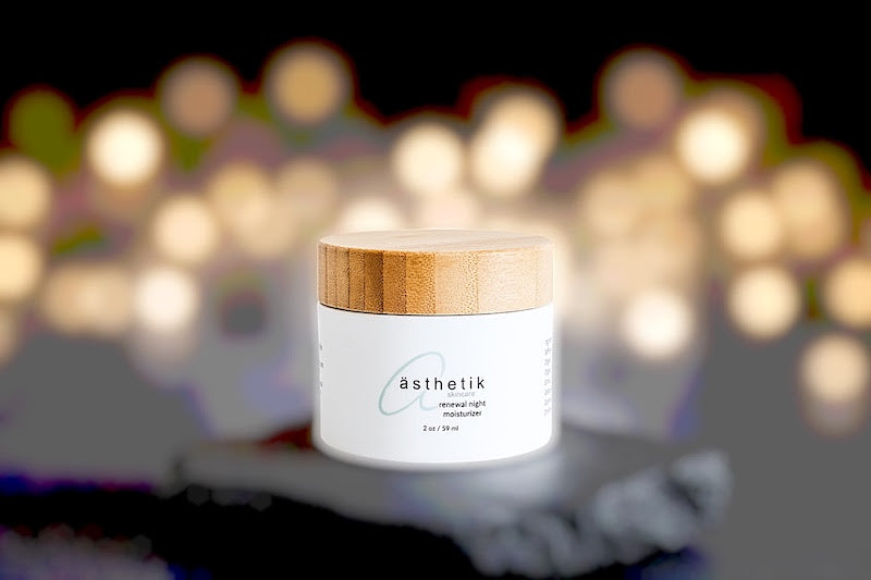 ästhetik skincare renewal night moisturizer on a black stone with blurred out sparkly lights in the background