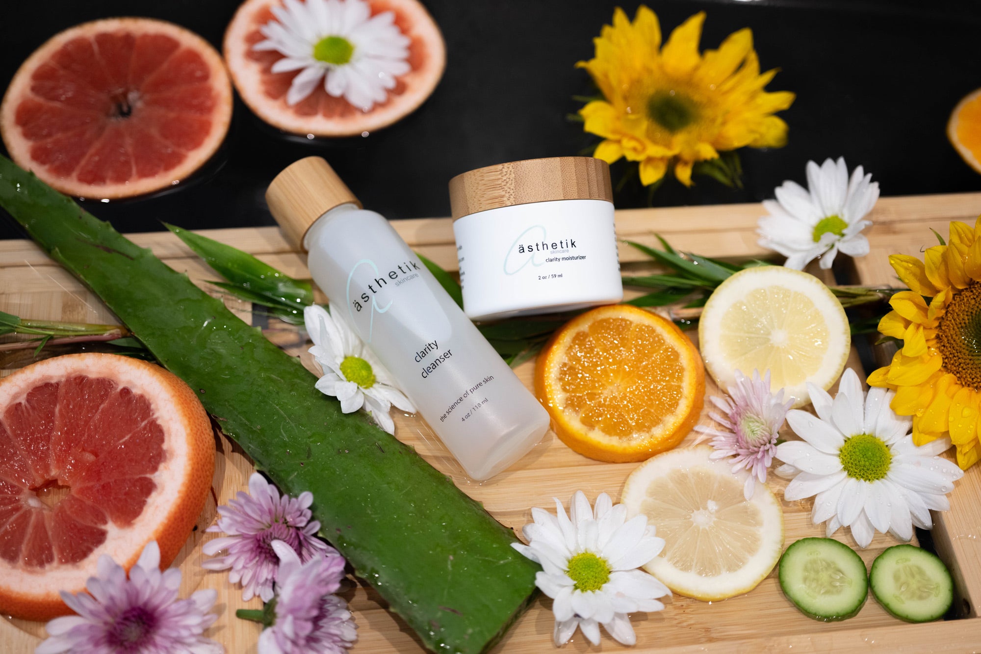 asthetik skincare clarity cleanser and clarity moisturizer on wooden tray with fruits and vegetables