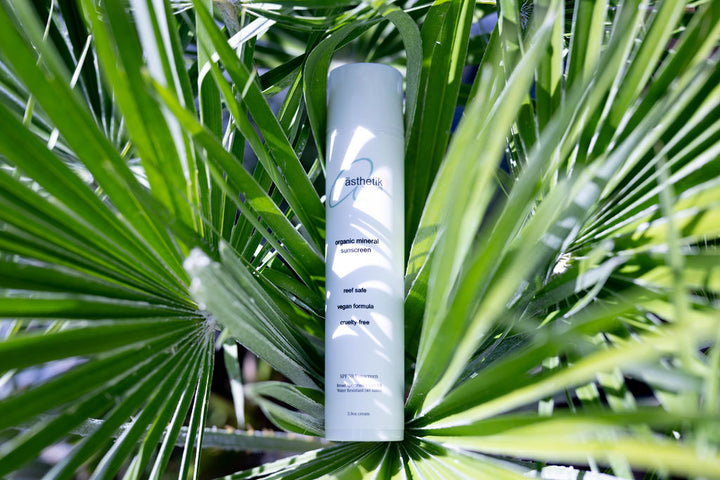 Organic tinted mineral sunscreen SPF 50 by ästhetik skincare, surrounded by lush green palm leaves