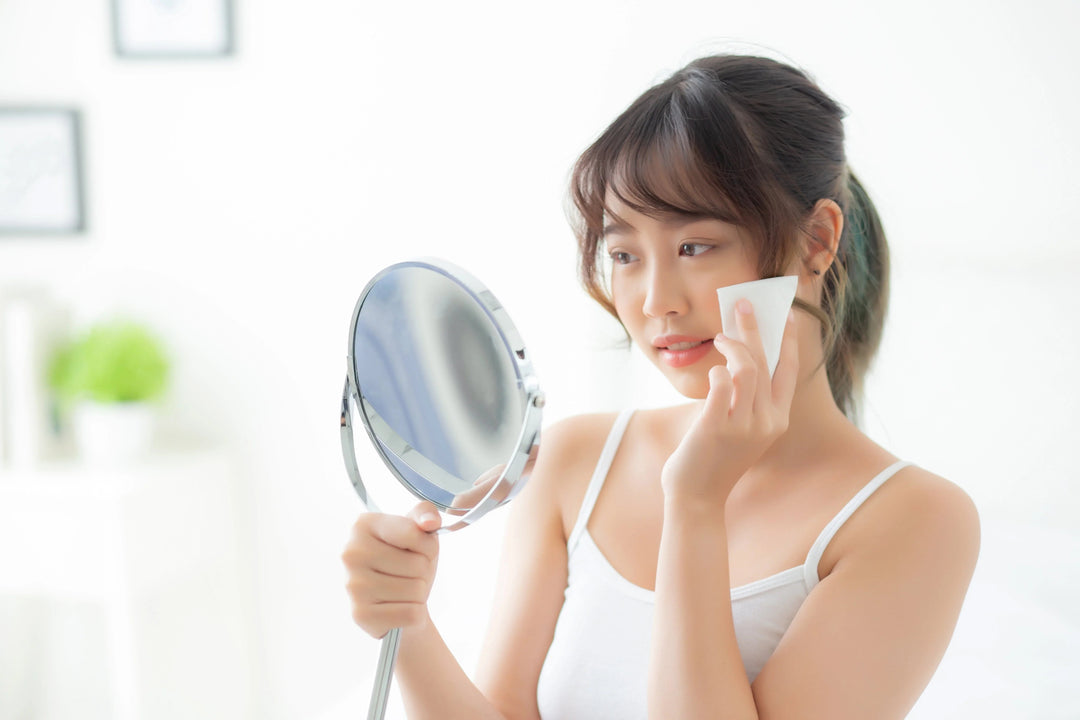 Young woman with clear skin using a cotton pad and handheld mirror in bright skincare routine