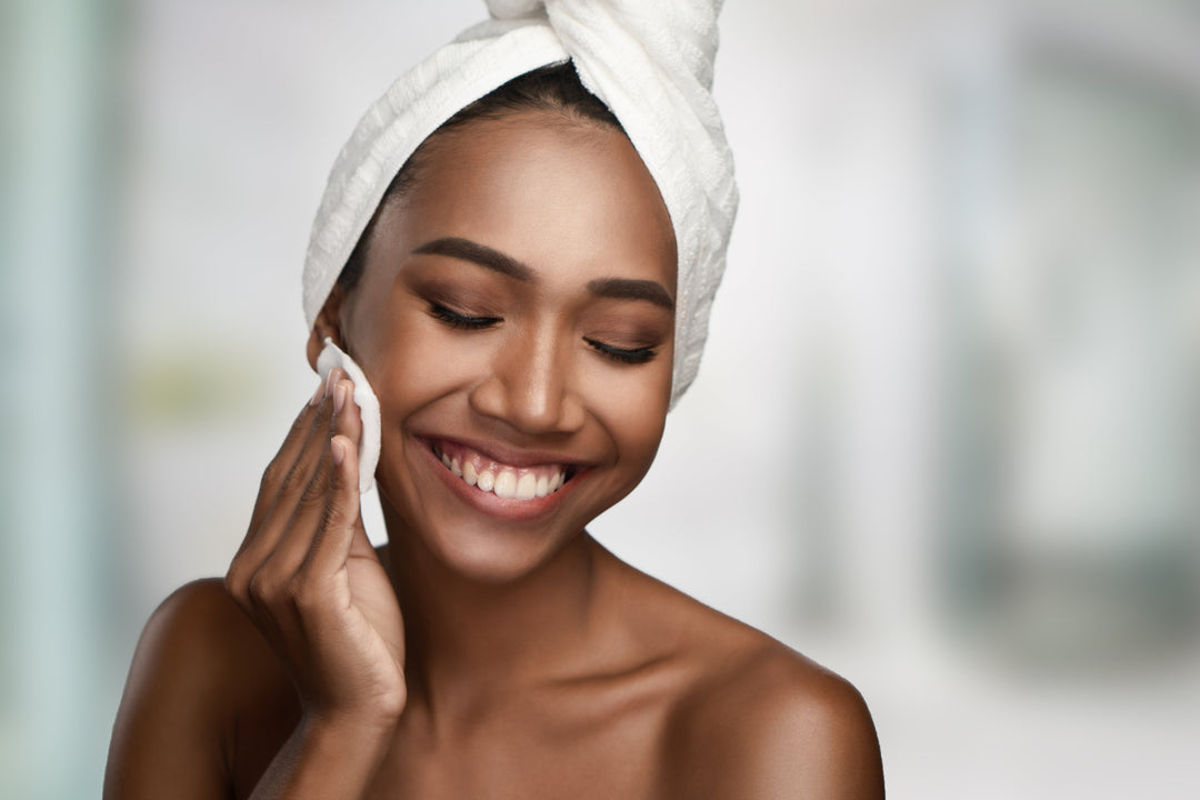 Close-up portrait of a beautiful smiling woman with clean skin cleaning her face with cotton swab pad isolated on bright background. 