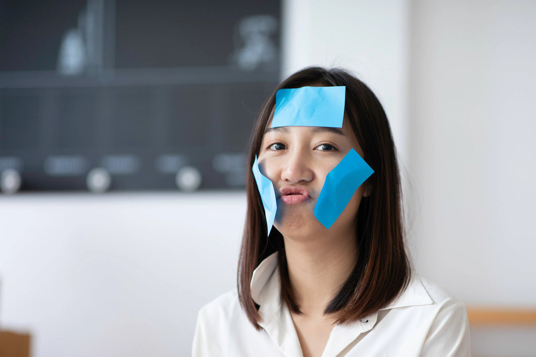 Woman with blue sticky notes on face, puckering lips, natural skincare fun moment in bright room