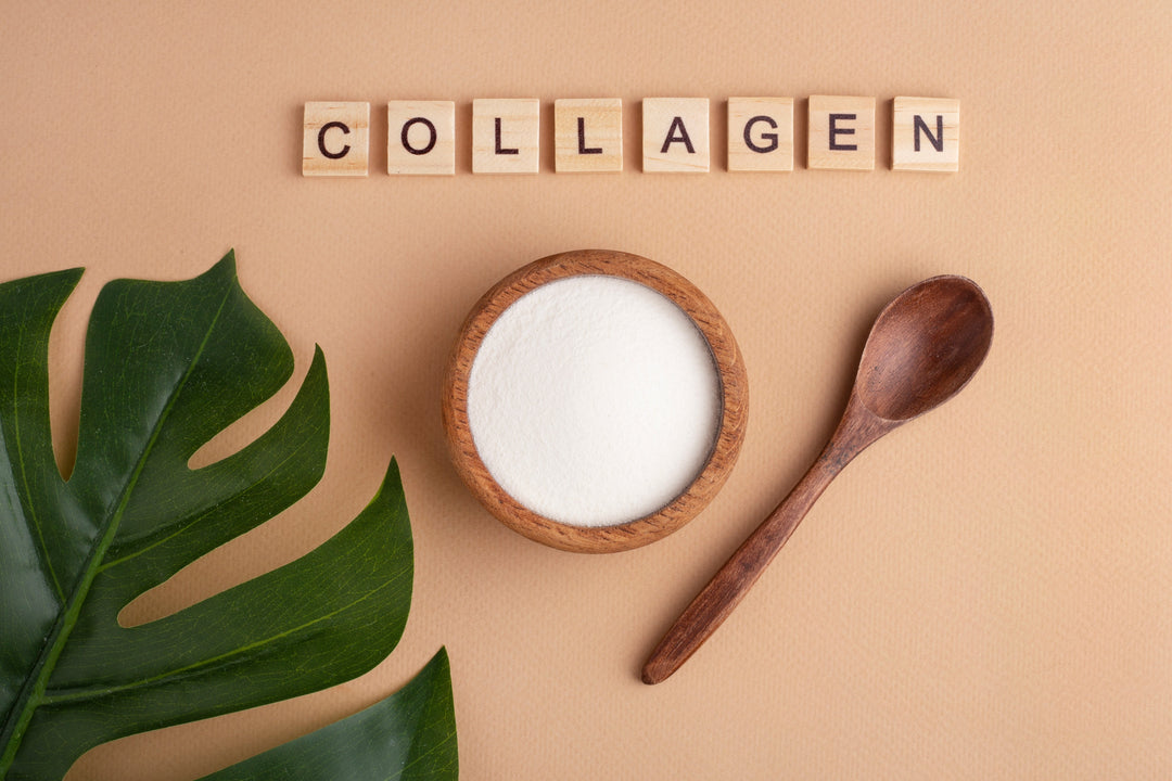 The word collagen spelled out on wooden tiles above a green leaf and a wooden spoon and bowl, which contains collagen powder.
