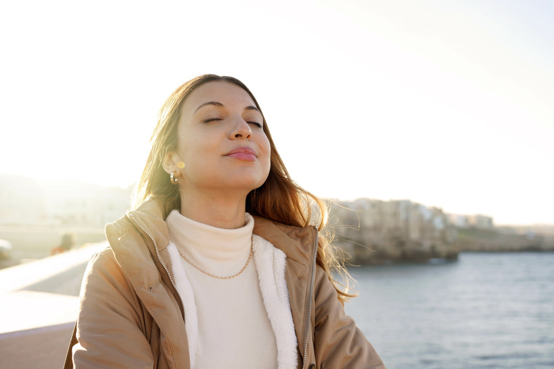 Portrait of young charming woman in winter clothes breathing fresh air relaxing with closed eyes and basking in the sun while on the beach