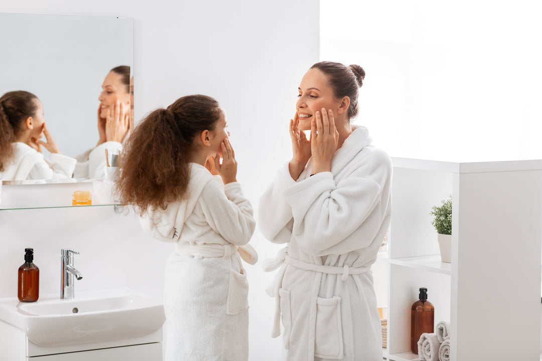 beauty, hygiene, morning and people concept - happy smiling mother and daughter touching their faces in bathroom