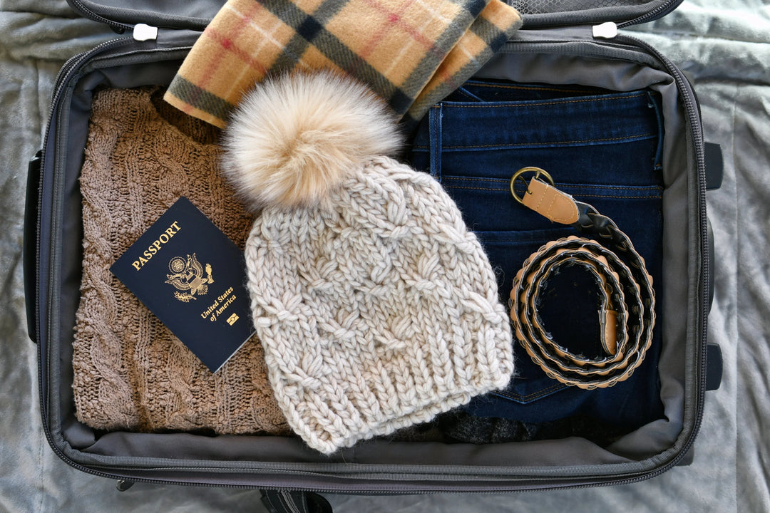 Open suitcase with neatly packed cozy winter clothes, US passport, knit hat, plaid scarf, jeans, and belt for travel
