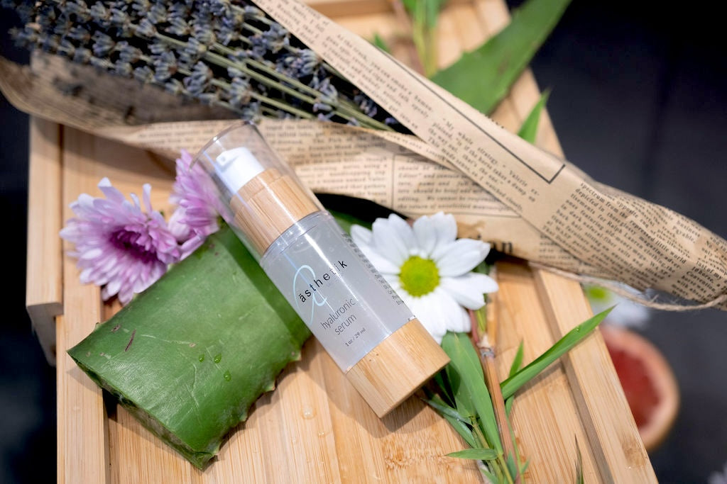 ästhetik skincare hyaluronic serum on a wooden bath board surrounded by flowers and aloe