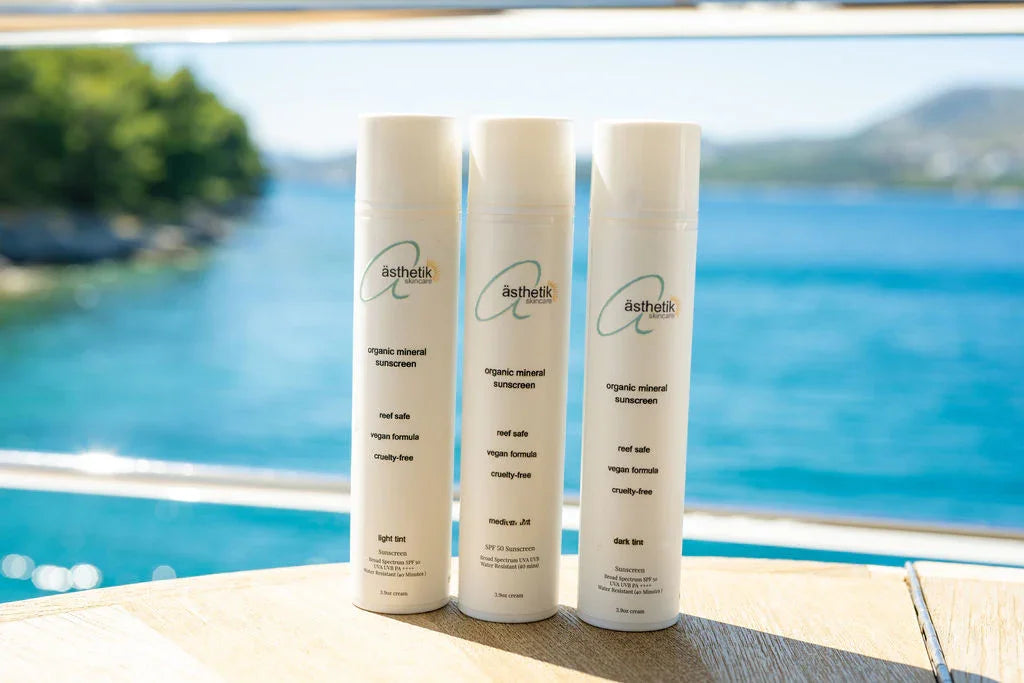 Three bottles of ästhetik organic mineral sunscreen on a sunny ledge by the ocean.