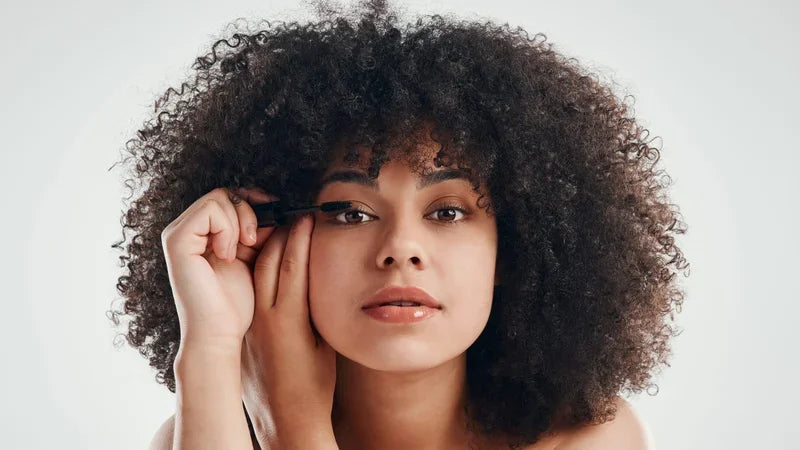 Woman with curly hair applying mascara to her lashes for a beauty look.