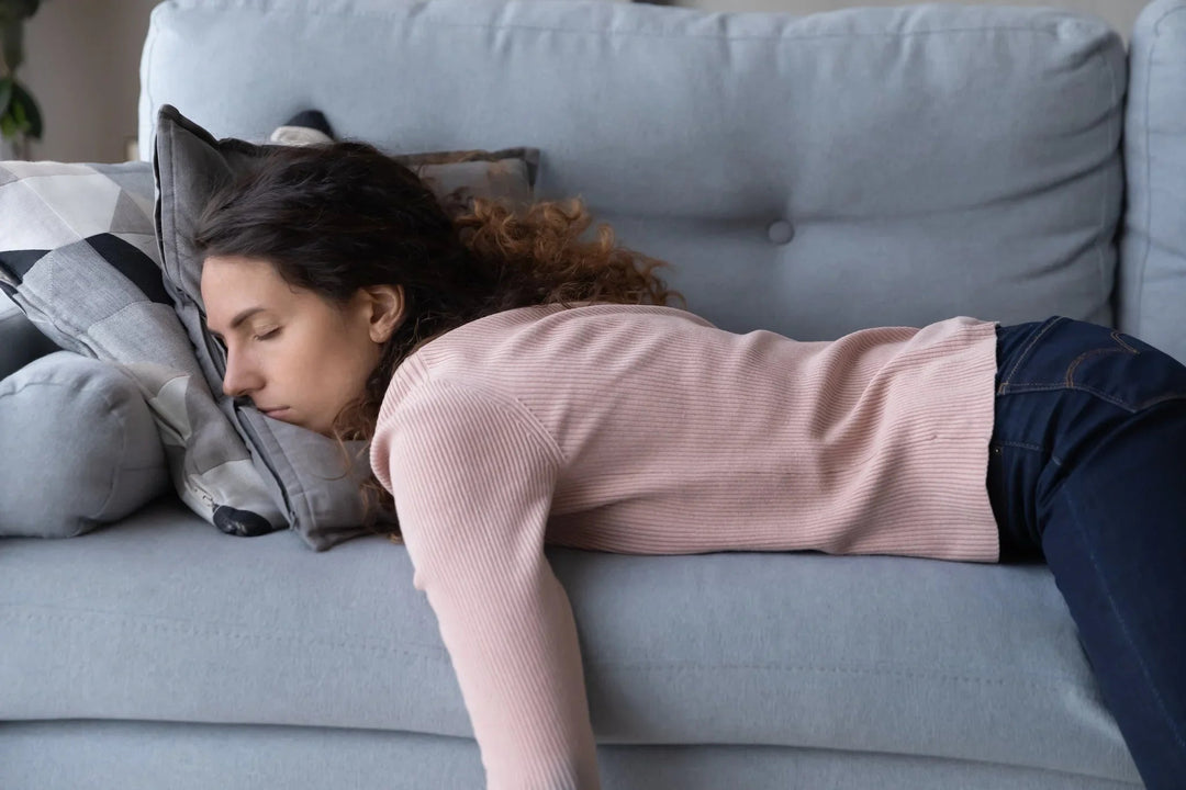 Woman in a pink sweater resting her head on a pillow on a light blue sofa.