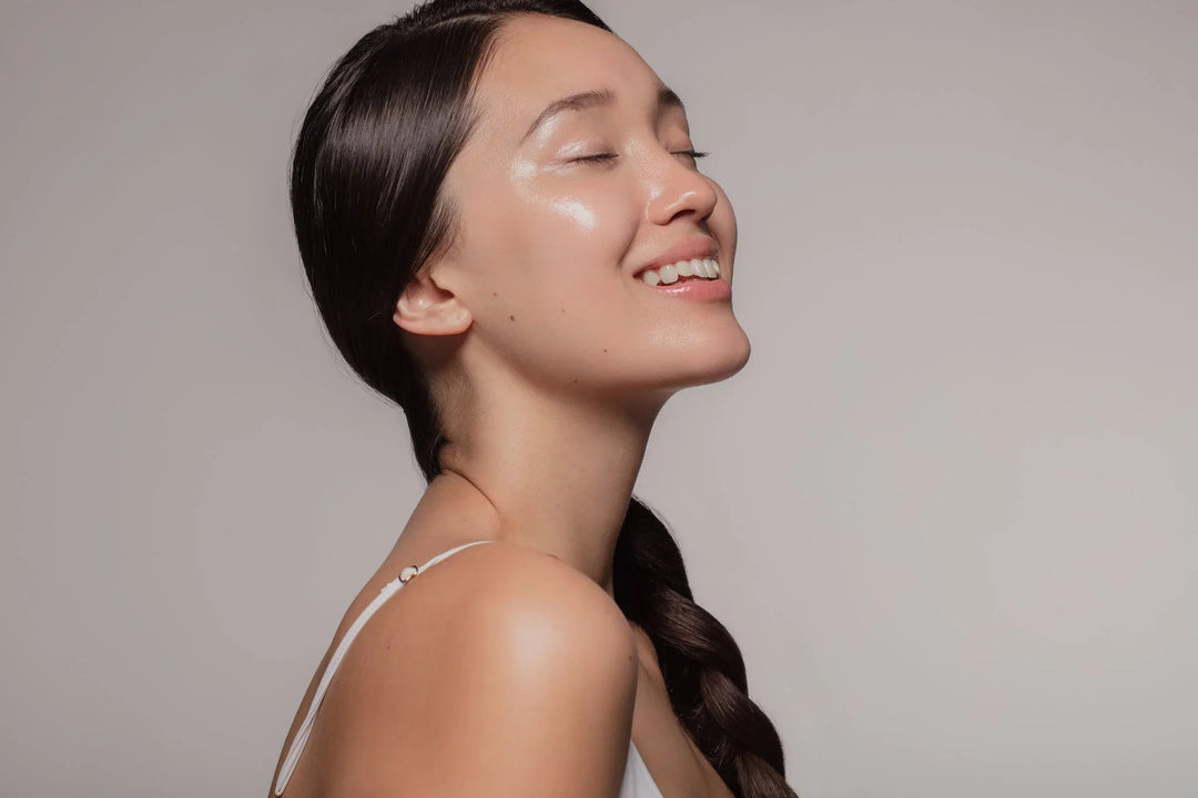 Side profile of a woman with glowing, hydrated skin smiling with closed eyes.