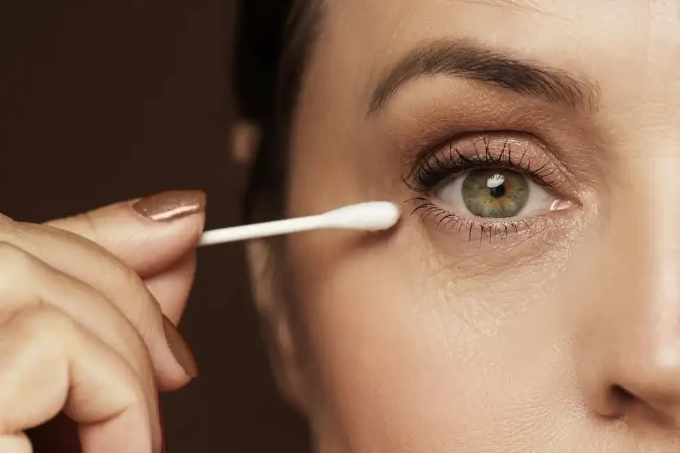 Close-up of a person using a cotton swab for precise eye area skincare application.