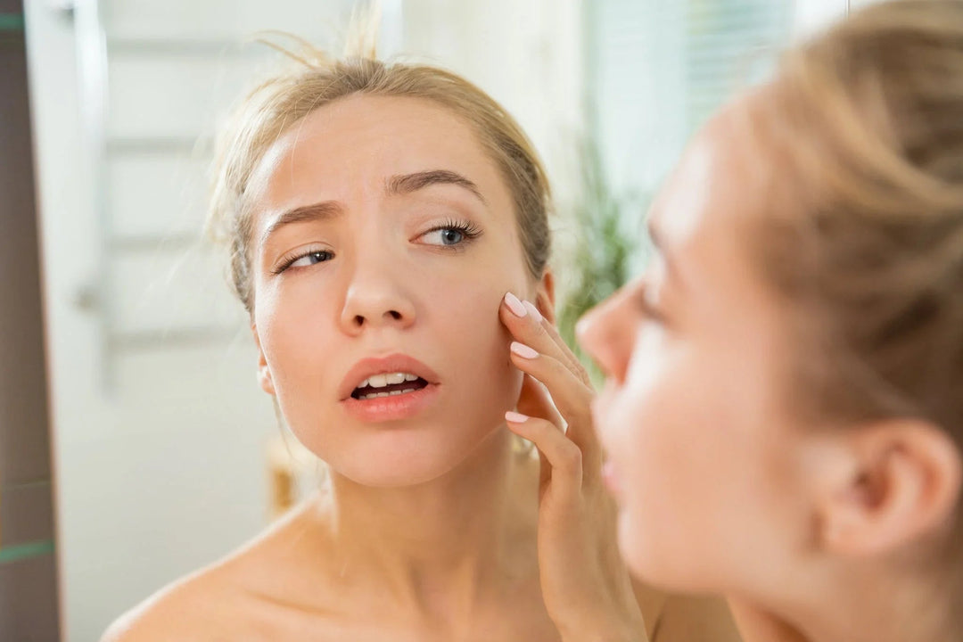A woman looking in the mirror while examining her skin for blemishes.