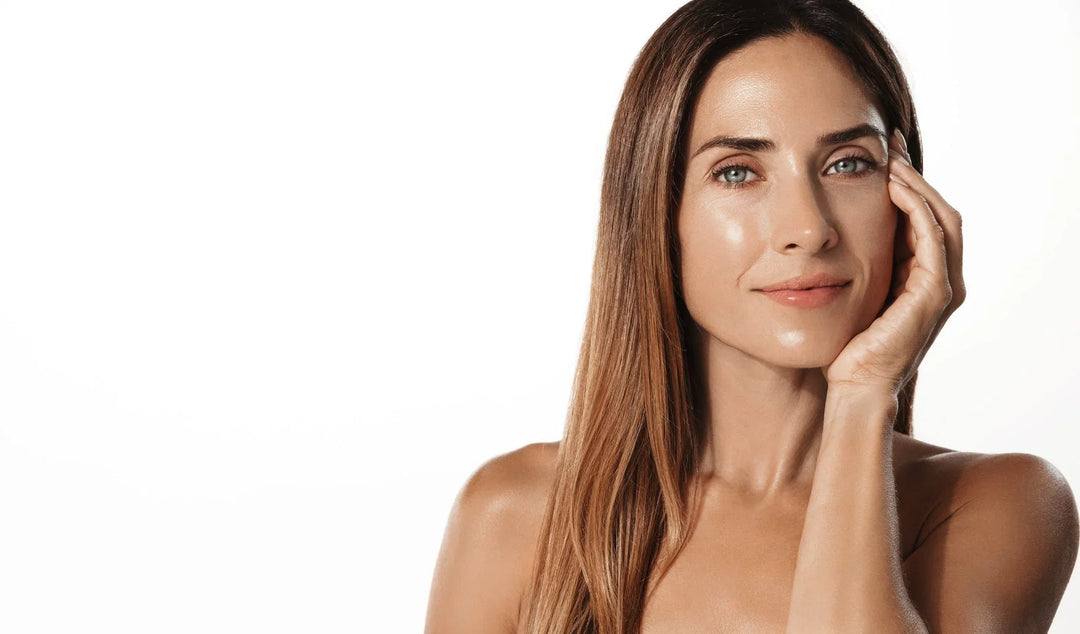 Portrait of a woman with glowing, hydrated skin touching her face against a white background.