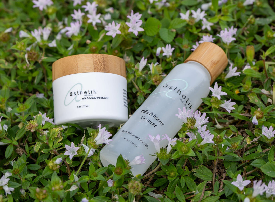 Ästhetik skincare milk and honey cleanser and moisturizer sitting on ground cover with small purple flowers
