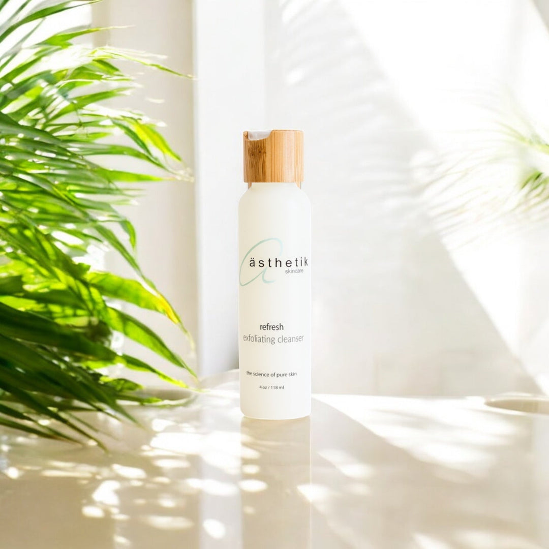 asthetik skincare refresh exfoliating cleanser on a white table with a white background and a green plant behind it