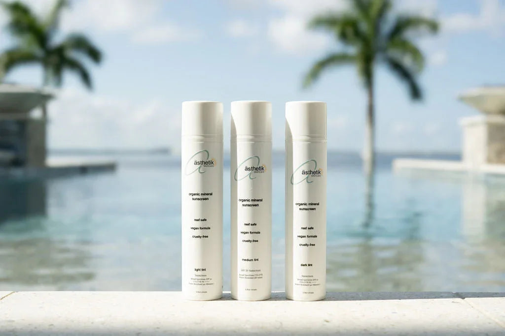 Three bottles of ästhetik organic mineral sunscreen in different tints by a sunny pool.
