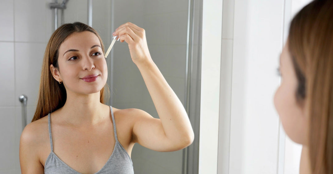 A happy young woman looking in a mirror and apply a serum to her face