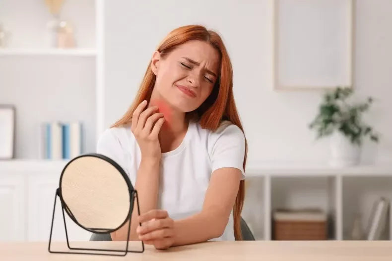 Woman with red hair touching her neck in pain, looking into a vanity mirror.