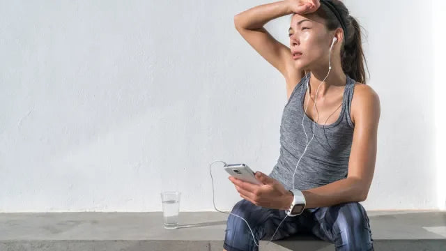 Sweaty woman in athletic wear resting with a smartphone and water after a workout.