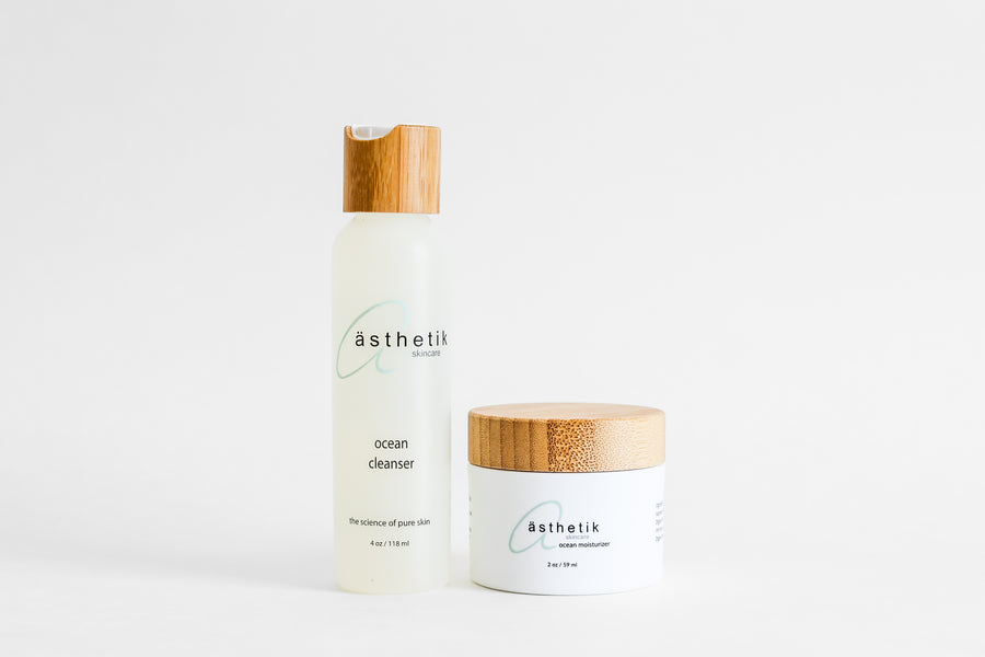 A bottle of ästhetik skincare ocean cleanser next to a jar of ästhetik skincare ocean moisturizer against a white background, both with wooden caps and branded with "asthetik skincare.