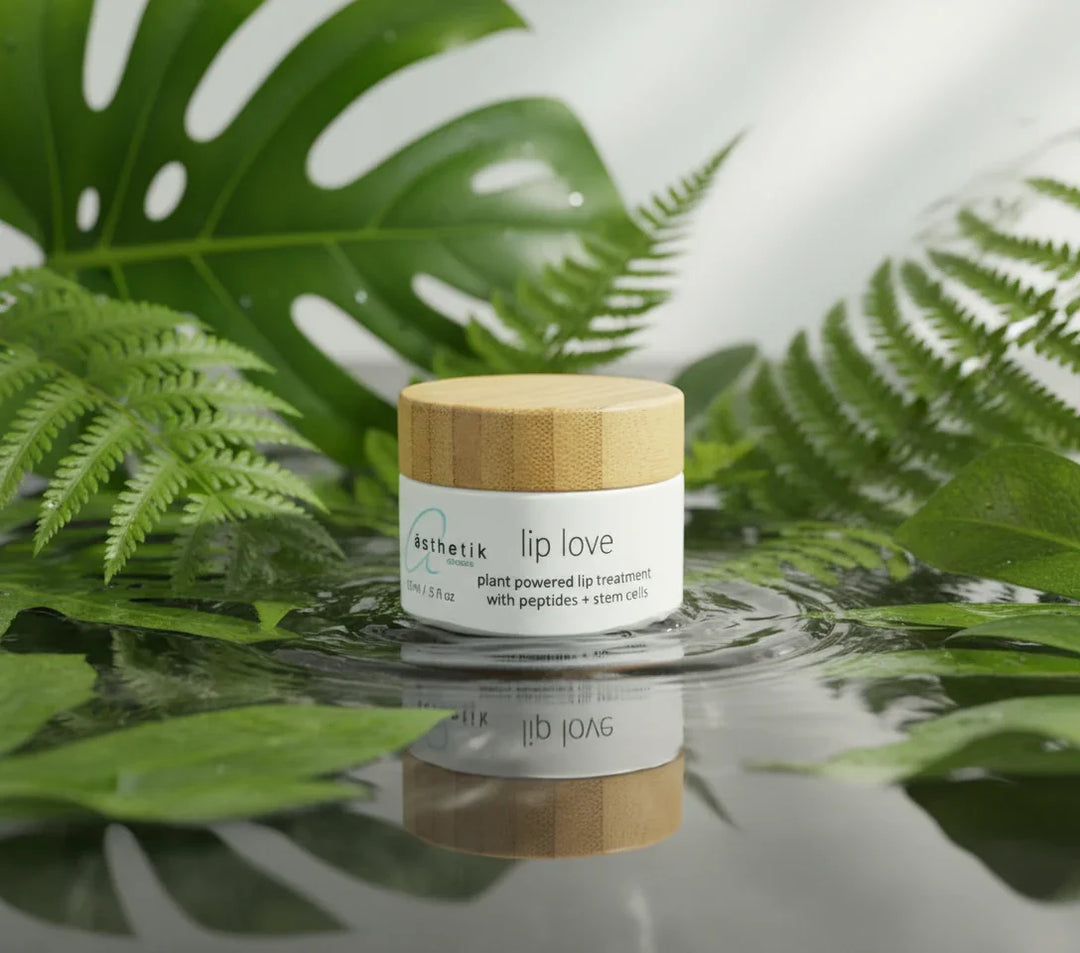 Jar of 'lip love' lip balm with wooden cap on water surrounded by green leaves