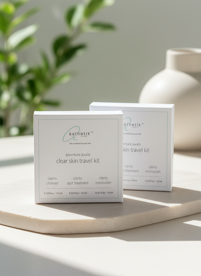 Two ästhetik clear skin travel kits on a stone tray with a plant in the background.