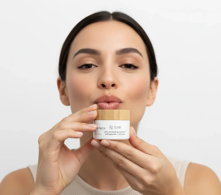 Woman holding a lip balm container with a plain background