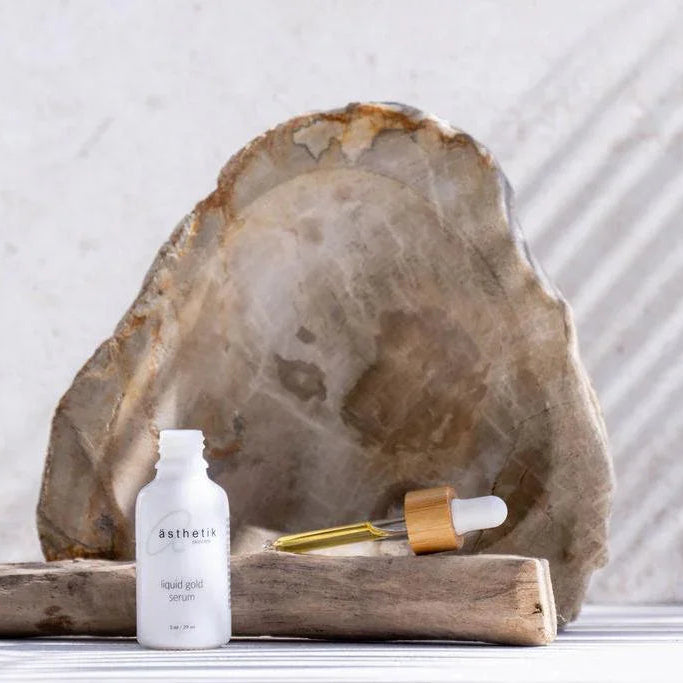A bottle of ästhetik skincare's liquid gold serum on a wooden block table.