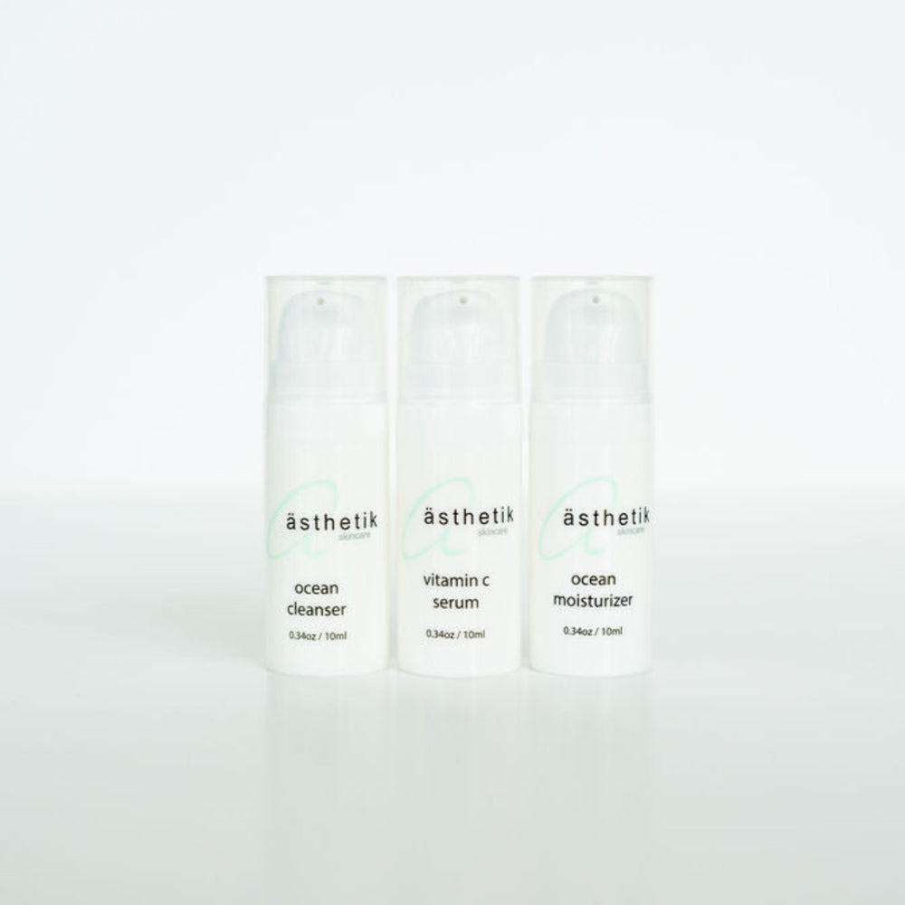 Three skincare product bottles labeled "ästhetik" lined up on a white surface, featuring Ocean Cleanser, Vitamin C Serum, and Ocean Moisturizer. This ästhetik skincare travel set is perfect for maintaining your routine on the go.
