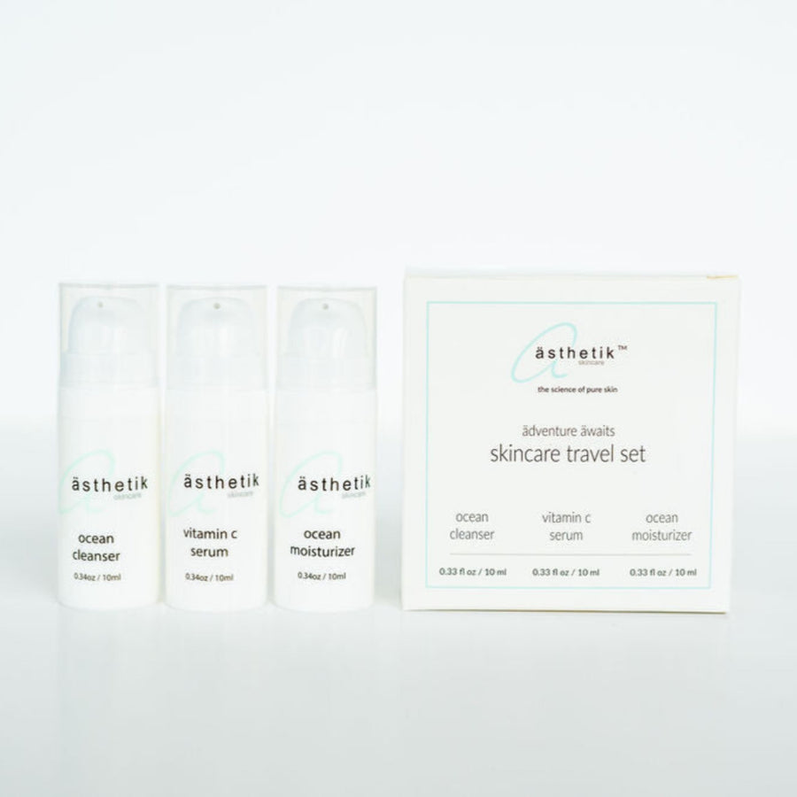 Image of a skincare travel set from "ästhetik skincare" including three small white bottles labeled "ocean cleanser," "vitamin C serum," and "ocean moisturizer," next to a box with corresponding labels.