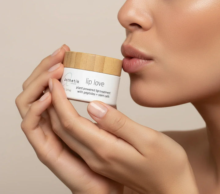 Person holding a container of 'lip love' lip balm close to their lips against a neutral background
