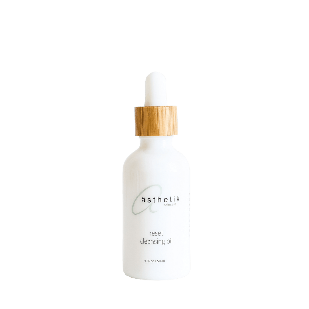 Elegant white cleansing oil bottle with a bamboo-colored cap from ästhetik skincare brand, featured against a solid green background.